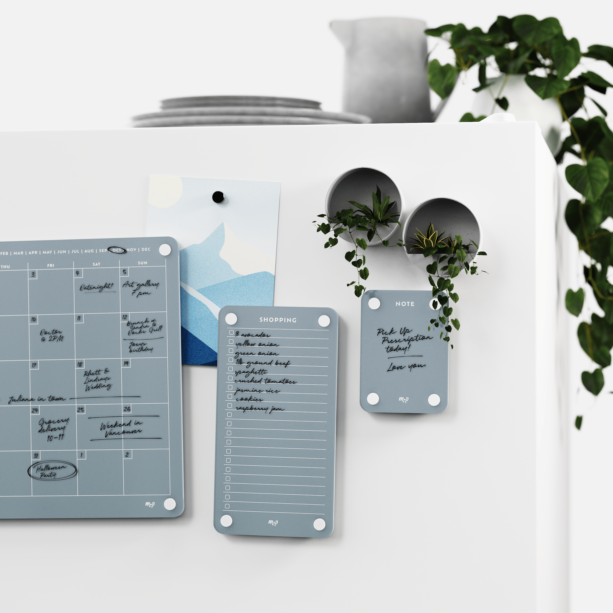 Slate grey calendar, shopping list and note board on a white wall beside two magnetic planters